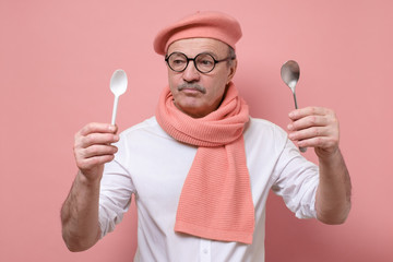 Zero waste concept. Senior funny caucasian man making choose between plastic and metal spoon standing over isolated blue background.