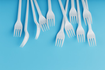 White plastic forks of disposable tableware on a blue background.