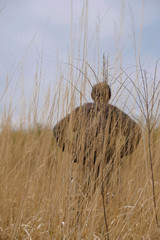 Silhouette of a man in black clothes behind tall dry grass in the wild in Ukraine.  On the back of the walker is a black backpack. Copy space.