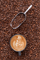 Cup of tasty cappuccino and scoop on coffee beans, top view