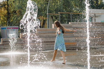 Girl in a blue dress having fun among the fountains