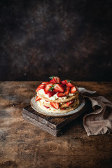 cake with fresh strawberries and cream cheese on wooden board, rustic wooden background, seasonal dessert
