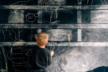 child drawing with colored chalks on the wall in the house - focus on the wall