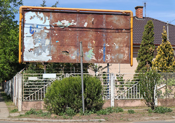 Old rusty ruined billboard next to a house