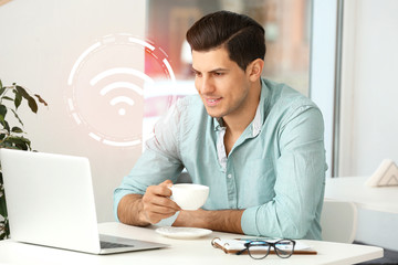 Handsome businessman with laptop using wifi in cafe