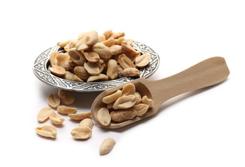 Roasted peanuts pile, savory snacks on metal plate, bowl with wooden spoon isolated on white background