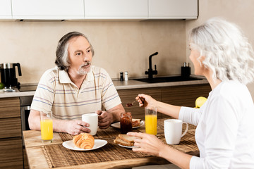 selective focus of bearded and mature man looking at wife near tasty breakfast