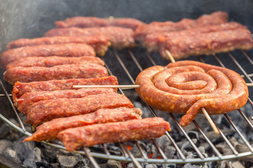 Sausages and traditional romanian sausages called ”mici” or ”mititei” (dish consisting of grilled ground meat rolls in cylindrical shape made from a mixture of meat and spices) on barbecue with smoke