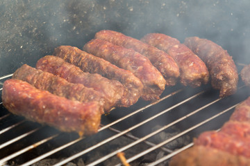 Sausages and traditional romanian sausages called ”mici” or ”mititei” (dish consisting of grilled ground meat rolls in cylindrical shape made from a mixture of meat and spices) on barbecue with smoke