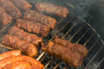 Sausages and traditional romanian sausages called ”mici” or ”mititei” (dish consisting of grilled ground meat rolls in cylindrical shape made from a mixture of meat and spices) on barbecue with smoke