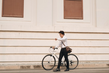 Young handsome guy with a bicycle on street, looking at watch.