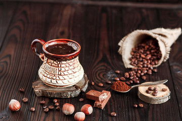 hot fragrant coffee in a vintage clay cup and coffee beans with nuts on a dark wooden background