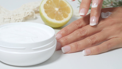 natural skin care, applying natural white cream on hands. Moisturizing treatment skin with natural ingredients Cream, lemon, officinal herbs. white background