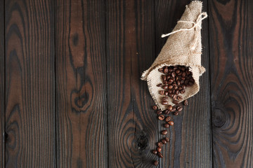 Roasted aromatic coffee beans on burlap, ground coffee in a spoon, on a dark wooden background