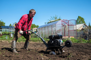 Old man plows the ground with a motor cultivator. A farmer ploughs the soil using a petrol cultivator.