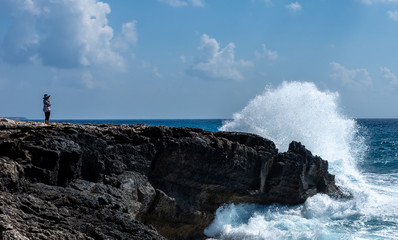 Fototapeta premium A girl on the beach watches the waves breaking on the rocky shore of the Mediterranean Sea on the Akamas Peninsula in the northwest of the island of Cyprus.