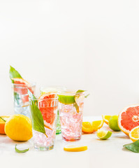 Glasses with iced citrus fruits  lemonade on white table with various ingredients. Summer drinks. Healthy  beverages.