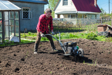 Old man plows the ground with a motor cultivator. A farmer ploughs the soil using a petrol cultivator.