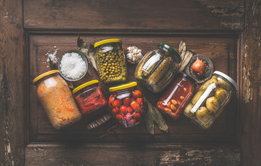 Homemade marinated and pickles vegetables preserve in jars on rustic wooden background with herbs...