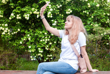 Young woman girl on a park bench uses a smartphone taking a selfie and communicating via video communication. Technology and modern lifestyle concept. A blogger makes outdoor content for his audience.