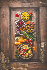 Obraz na płótnie Canvas Tasty vegetarian or vegan food cooking ingredient with pickled vegetables, olives , olives oil, green organic almonds lemon and figs on vintage wooden background with kitchen utensils. Top view.