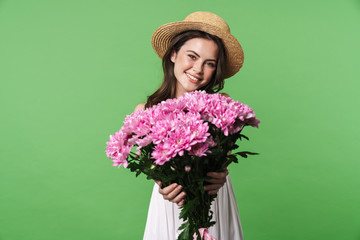 Image of cheerful pretty woman in straw hat smiling and holding flowers