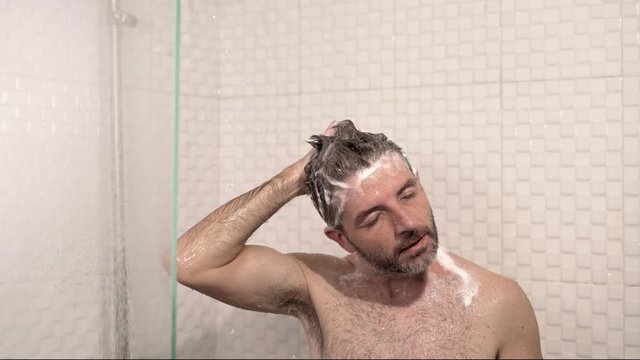 morning shower - lifestyle shot of young attractive and happy man with beard taking a shower at home washing his hair with shampoo enjoying cheerful in wellness and hygiene concept