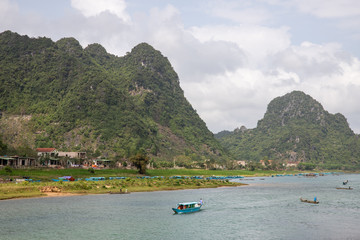 Song Son River with wooden boats on the water and docked boats on the background of the mountains in Phong Nha, Vietnam