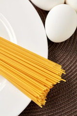 Uncooked raw spaghetti on a white plate with eggs