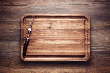 Empty vintage wooden cutting board with roast fork on wooden table