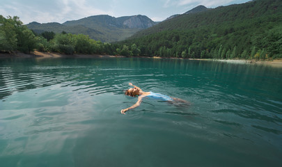 Traveler woman swimming on back in beautiful mountain lake with clear blue water against mountains. beautiful scenery, people in nature and travel concept