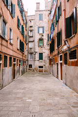 Close-ups of building facades in Venice, Italy. Dead end Venetian street. Five-story houses with blue-green wooden shutters on the windows, linen is dried in the windows, an old stone floor.