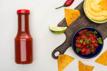top view of corn nachos with lime, chili, ketchup and cheese sauce on wooden cutting board on white background
