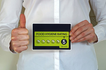 Restaurant manager or other kitchen worker with thumb up holds Food Hygiene Rating 5 sticker from The United Kingdom Food Standards Agency