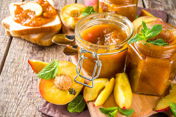 Homemade peach jam in different jars, with fresh organic peaches on wooden rustic background copy space