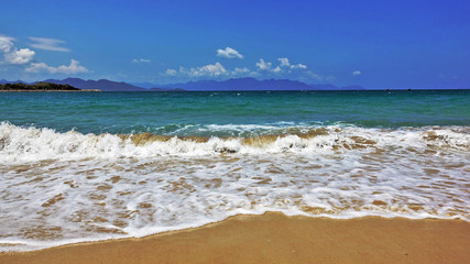 Vietnam. Summer. White lacy foam of waves lays beautifully on clean sand. Emerald Sea, blue sky. On the horizon are silhouettes of mountains and clouds. Relax Paradise.