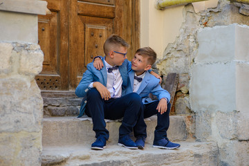 Two boy brothers in suits are sitting on the steps and hugging.