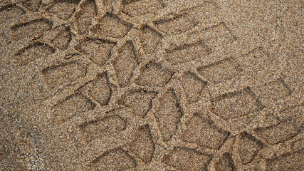 Tire prints on beach sand left by off-road vehicle. Abstract background and pattern.