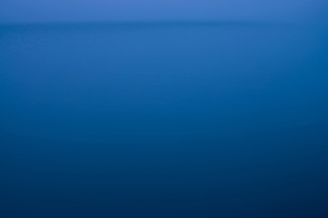 Water ripple nature background. Natural texture of sea of blue classic color. Deep blue calm water in dusk close-up. Meditative image of dense fog above lake. Soft light glitters on water surface.
