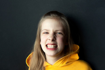 Teenager girl in an orange sweatshirt with bright emotions on her face on a black background. Anger, aggression on the face. Selective focus. Side view