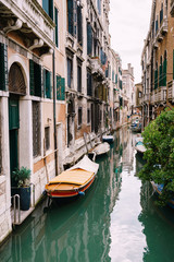 Moored boats at the walls of houses in the water in Venice. Narrow deserted canal between houses, azure sea water at the foot of the house.