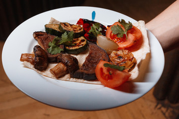 Grilled meat with vegetables served with pita on white plate