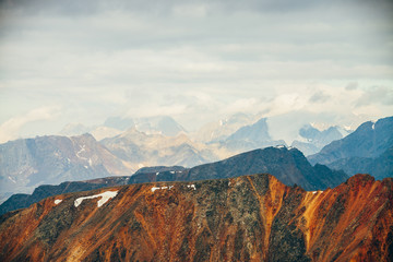 Atmospheric alpine landscape with red rockies in golden hour. Scenic view to big orange rocks and giant snowy mountains with glacier in sunrise. Wonderful highland scenery. Flying over mountains.