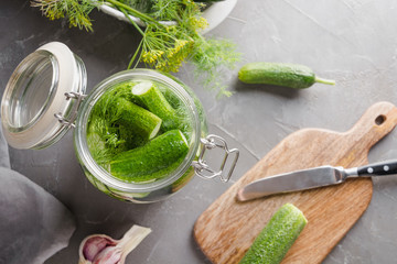 Pickling cucumbers in glass jar with mineral water, dill and garlic on grey. View from above.
