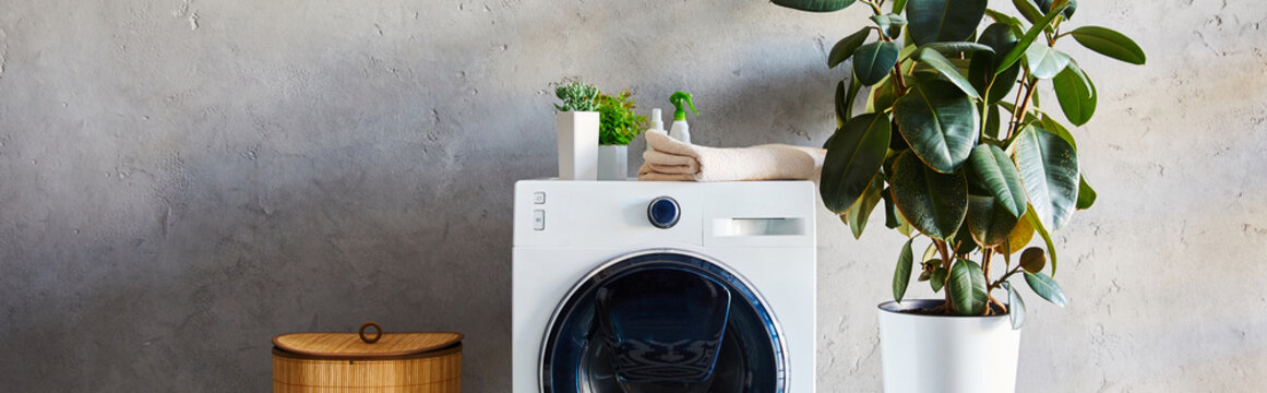 panoramic shot of plants, towel and bottles on washing machine near laundry basket in bathroom
