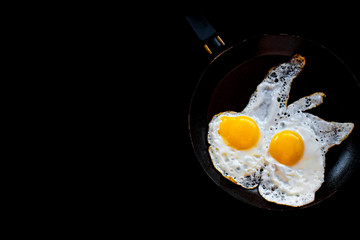 Fried eggs in a small black pan on a black background