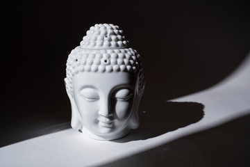Ceramic head of Buddha statue in the ray of light.