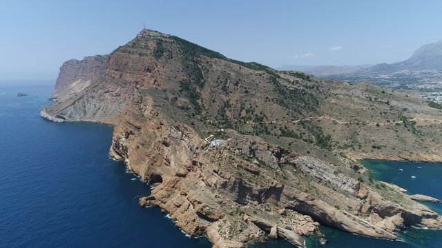 AERIAL DRONE SMOOTH BACKWARD SHOT OF STUNNING MEDITERRANEAN BLUE SEACOAST MOUNTAIN RANGE WITH CLIFFS, LIGHTHOUSE AND TURQUOISE COVE