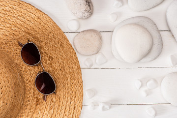 Top view of sunglasses on straw hat near sea stones on white wooden background
