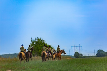 Young people horseriding in a field at spring. Blue sky above.
